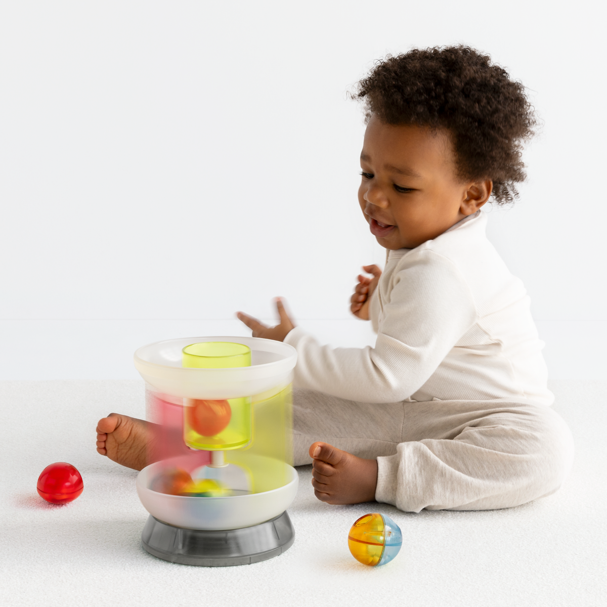 Side view of a toddler playing with a multi-colored translucent plastic toy carousel.