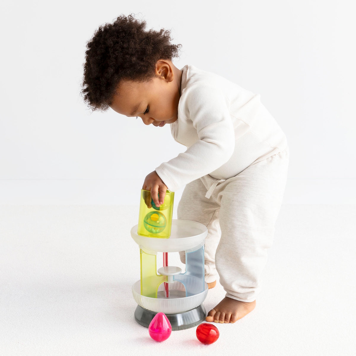 Side view of a toddler playing with a multi-colored translucent plastic toy carousel.