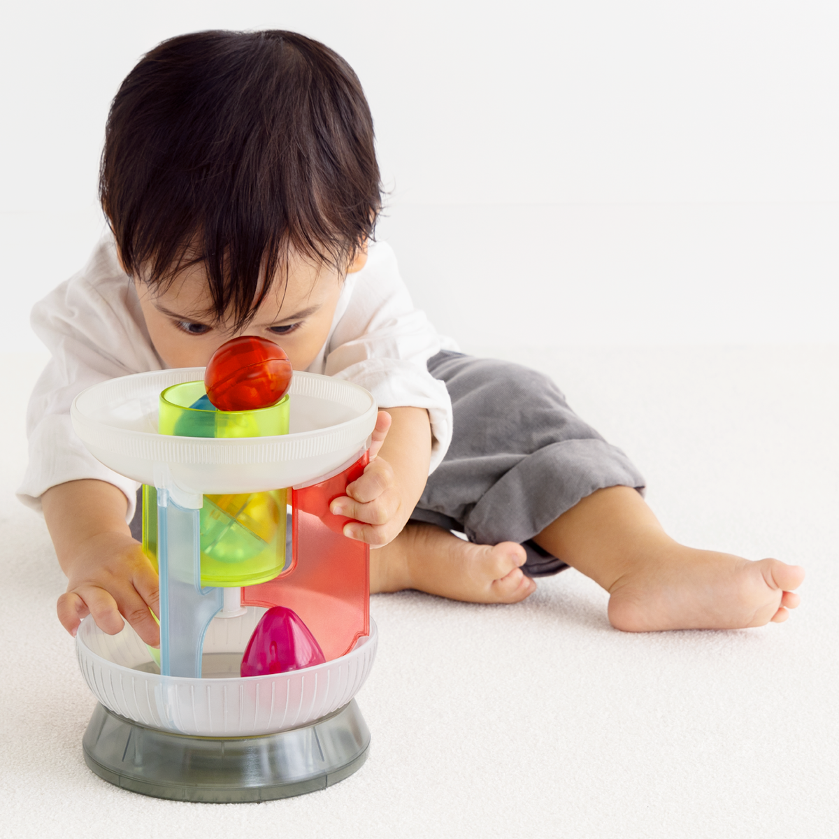 Front view of a toddler peering into a multi-colored translucent plastic toy carousel.