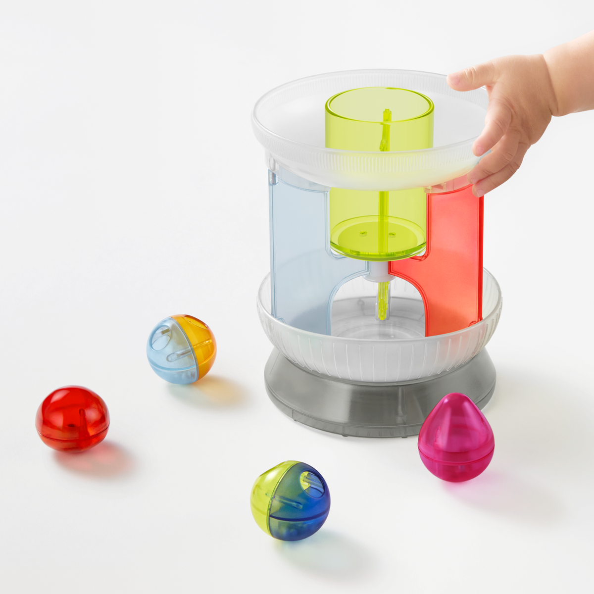 Angled front view of a multi-colored translucent plastic toy carousel with a child's hand on top.