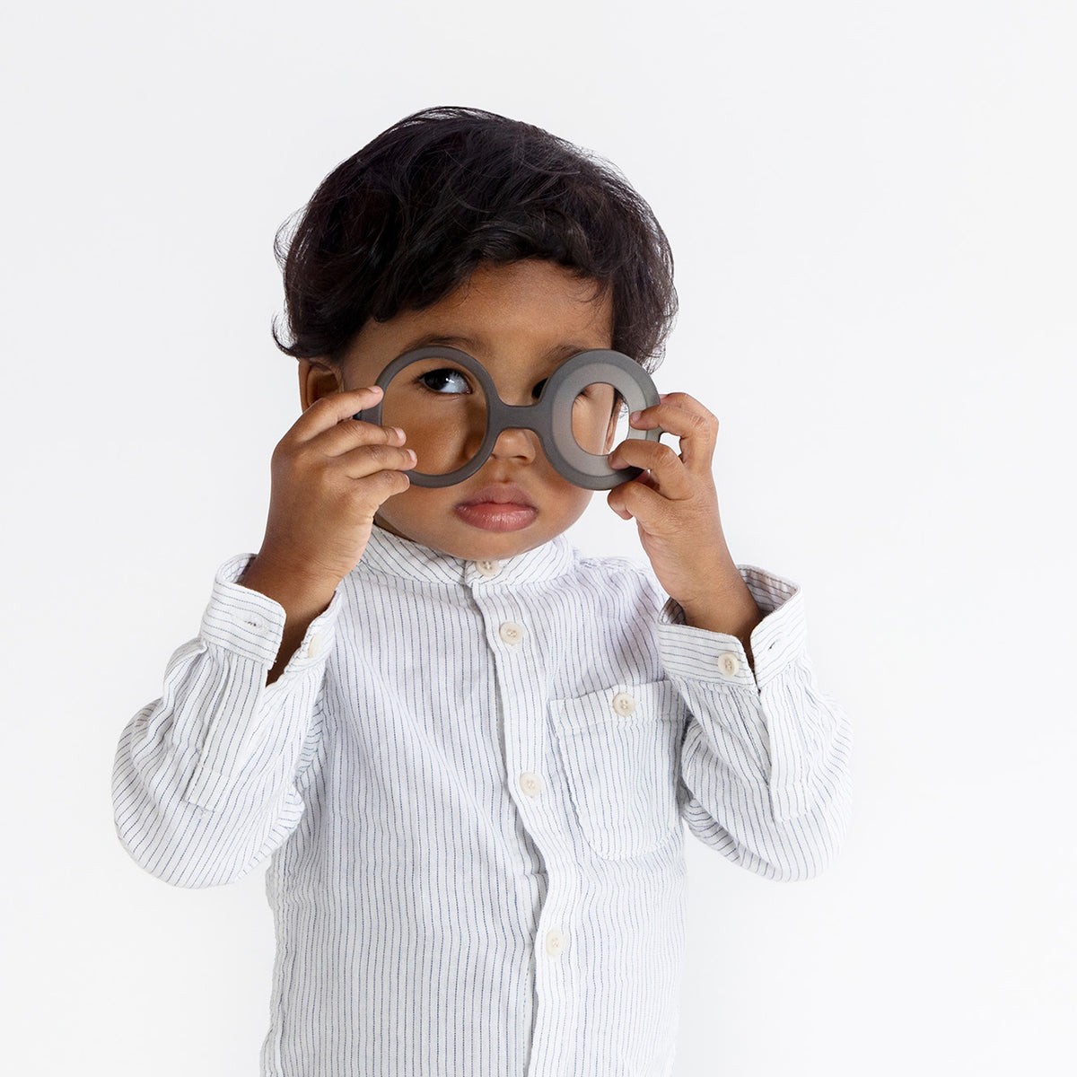Front view of a toddler trying on grey plastic toy glasses from a curiosity lantern set.