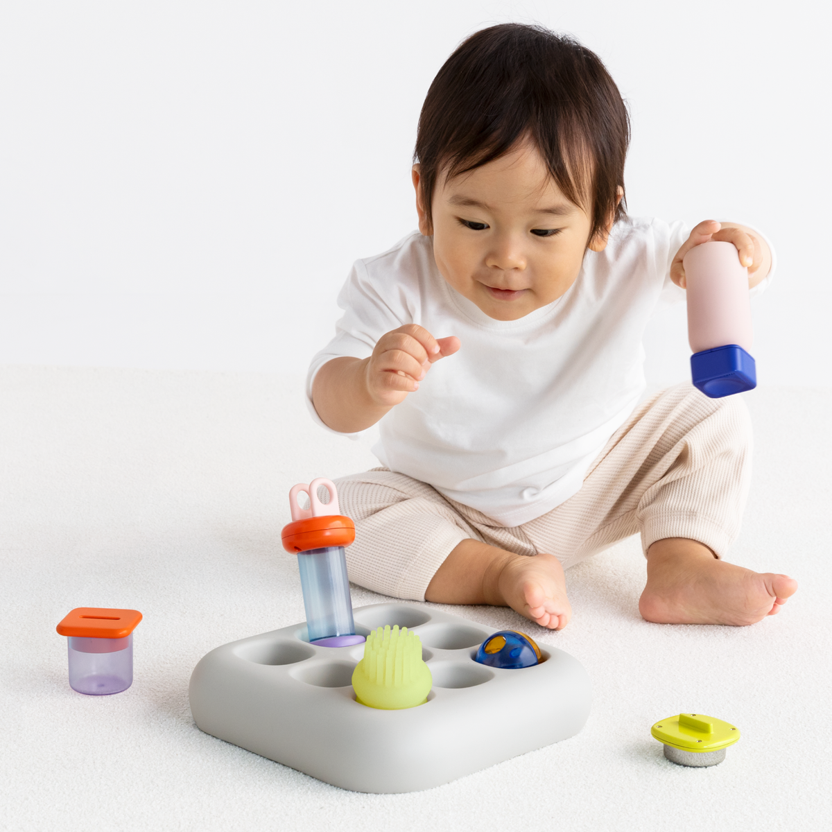 Front view of a baby playing with the light gray silicone Curiosity Nook toy with colorful pieces.