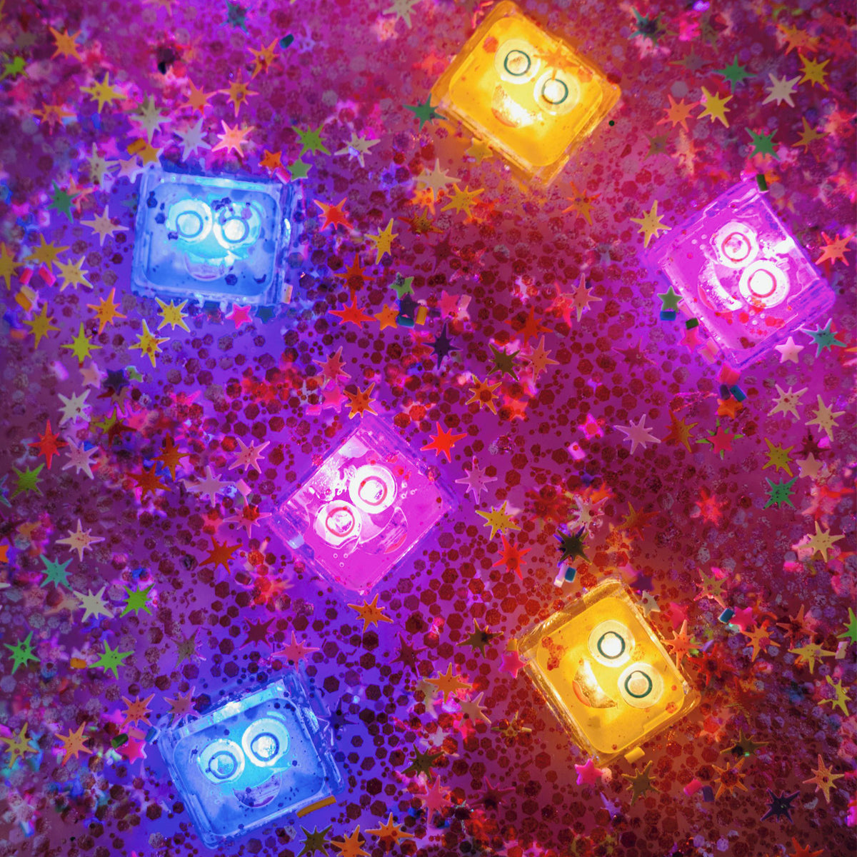 A vibrant mix of glowing Glo Pals cubes in blue, yellow, and purple, floating in water with shimmering star confetti.