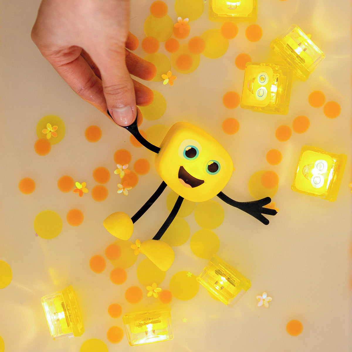 A yellow Glo Pals Alex character floating in water with glowing yellow light-up cubes and scattered yellow confetti.