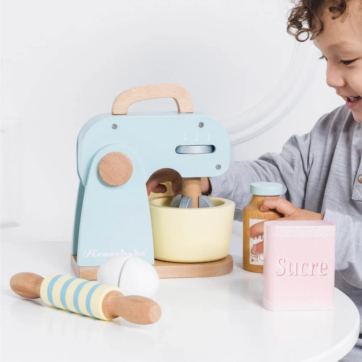 Child playing with a pastel blue wooden mixer set with accessories.