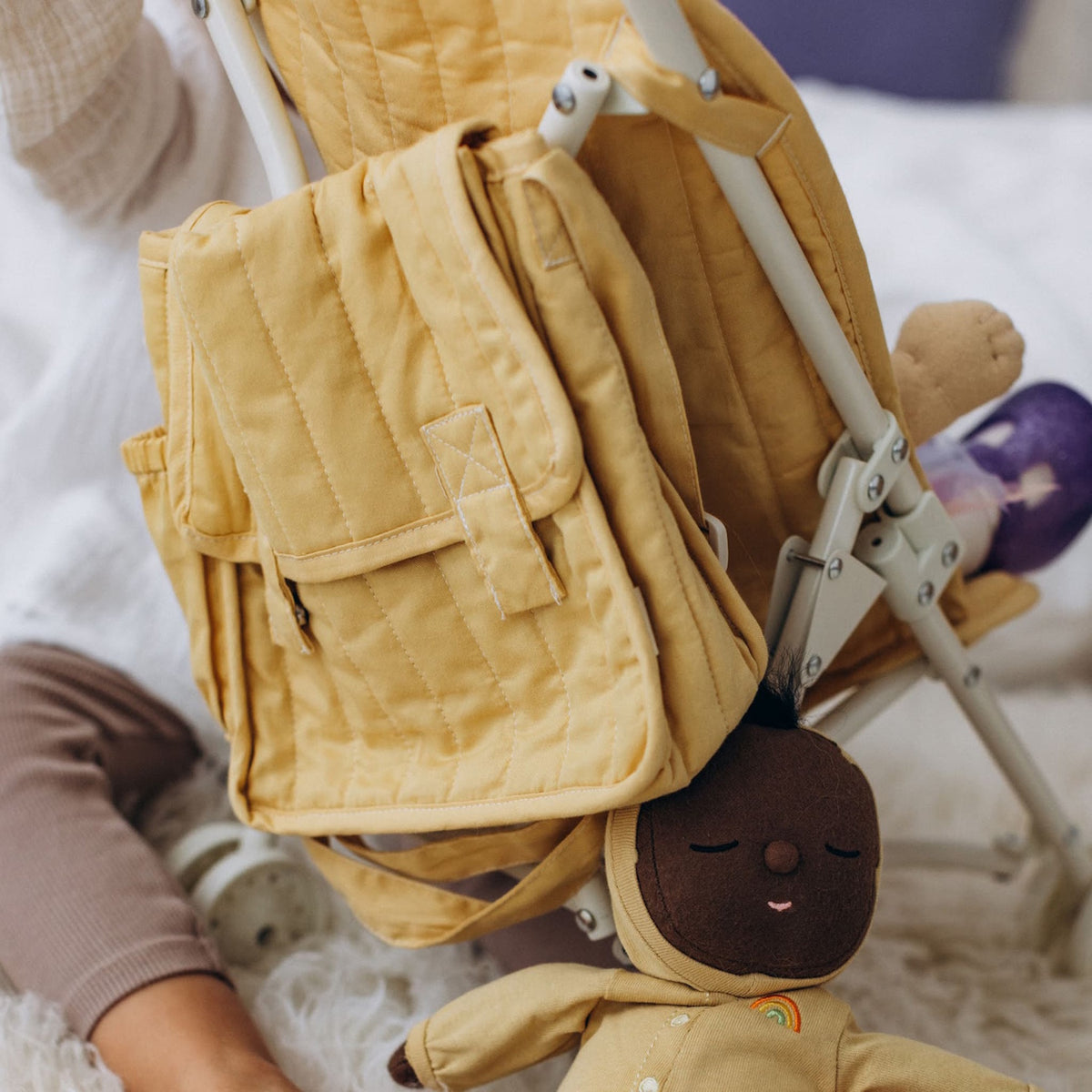 Honey-colored quilted diaper bag hanging on a doll stroller next to a plush baby doll.