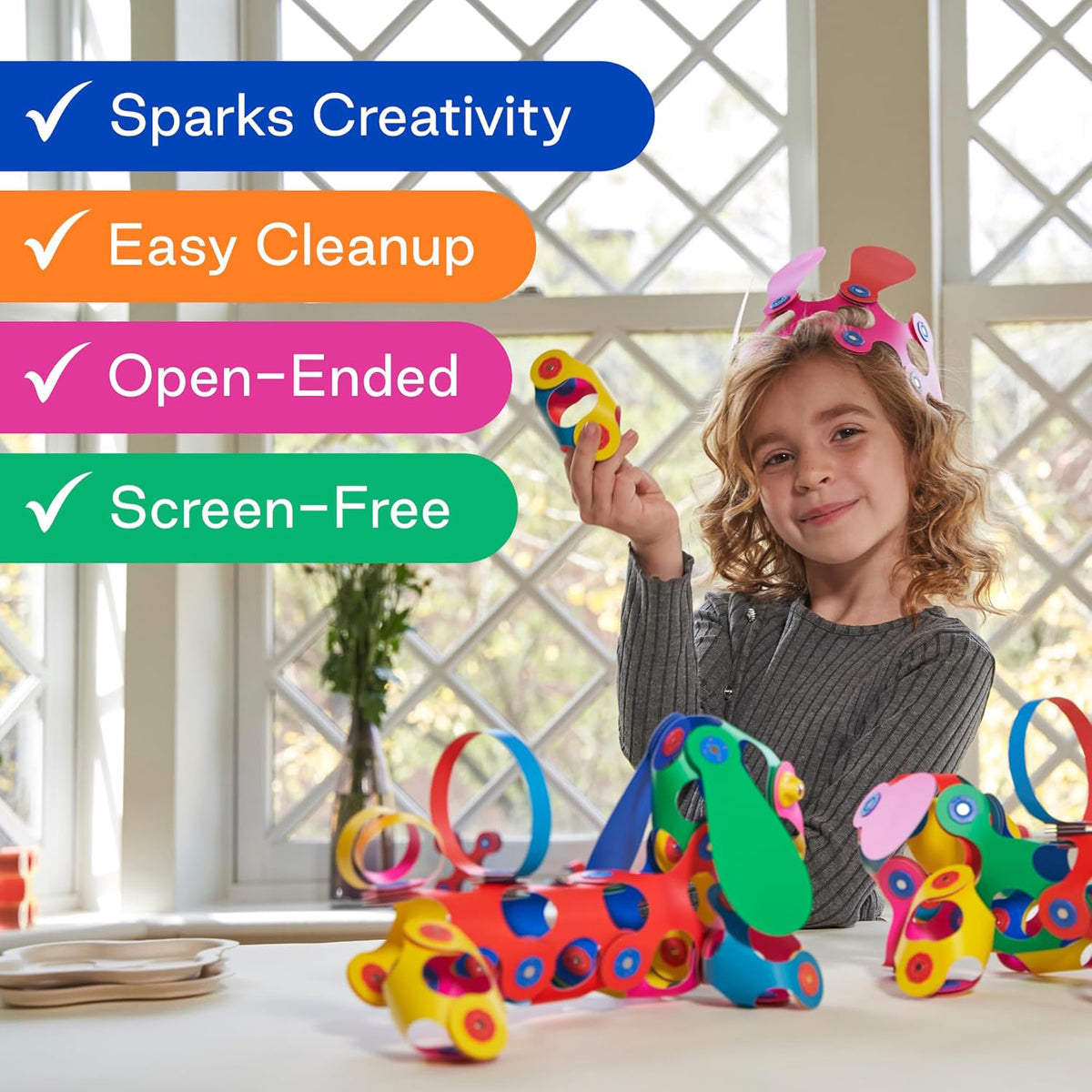 Young girl wearing a toy crown, holding up a magnetic piece near colorful creations with feature callouts.