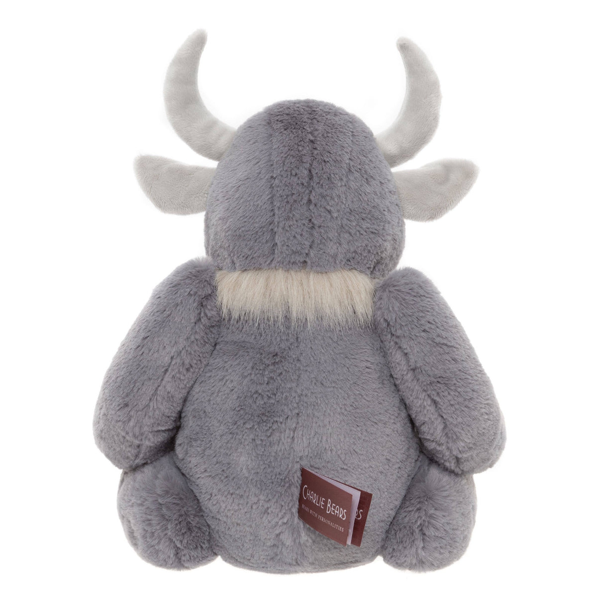 Back view of a plush grey horned creature toy sitting down, showing curved horns, soft fur, and a fabric tag.