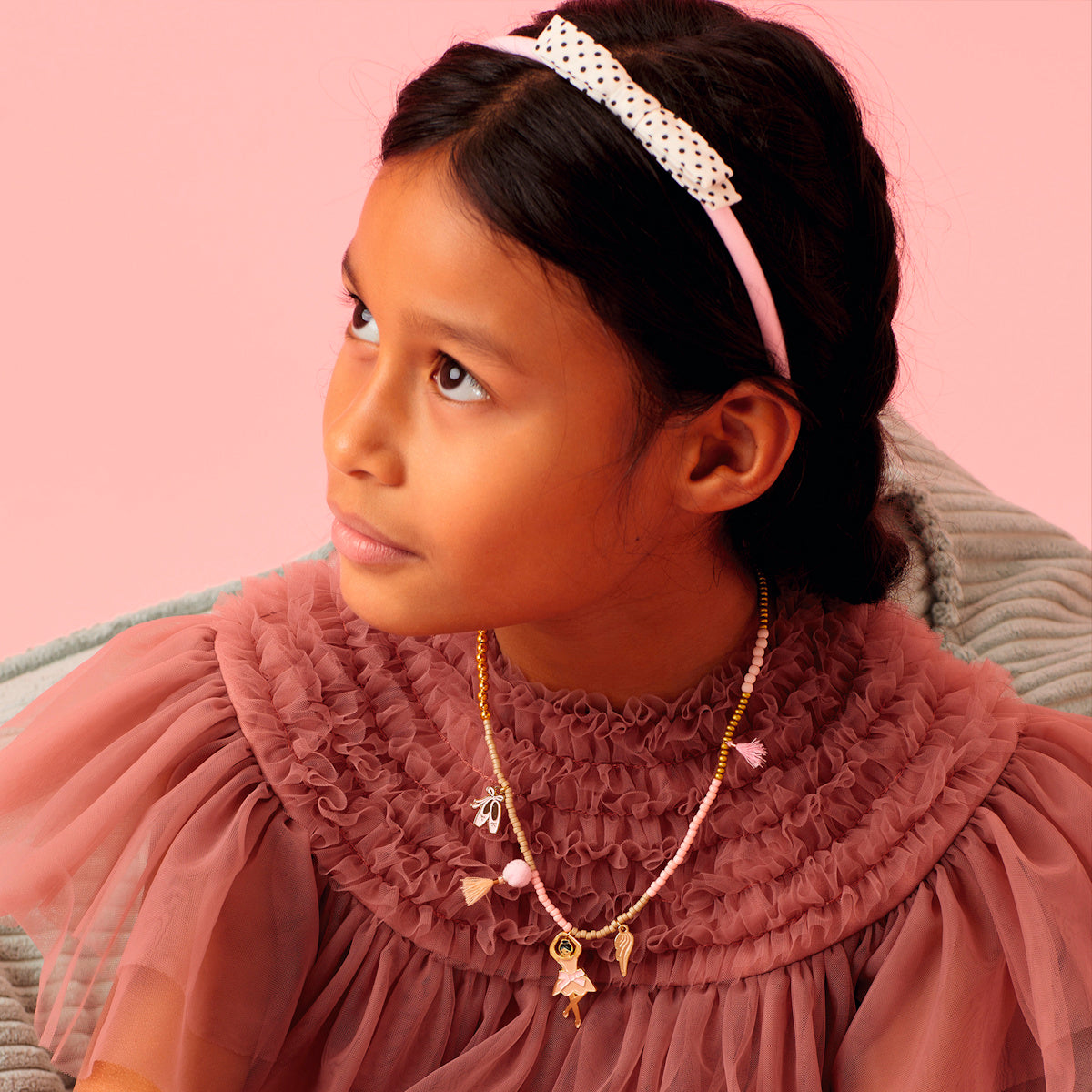 Girl wearing dance collection ballerina charm necklace and polka dot bow headband in pink.