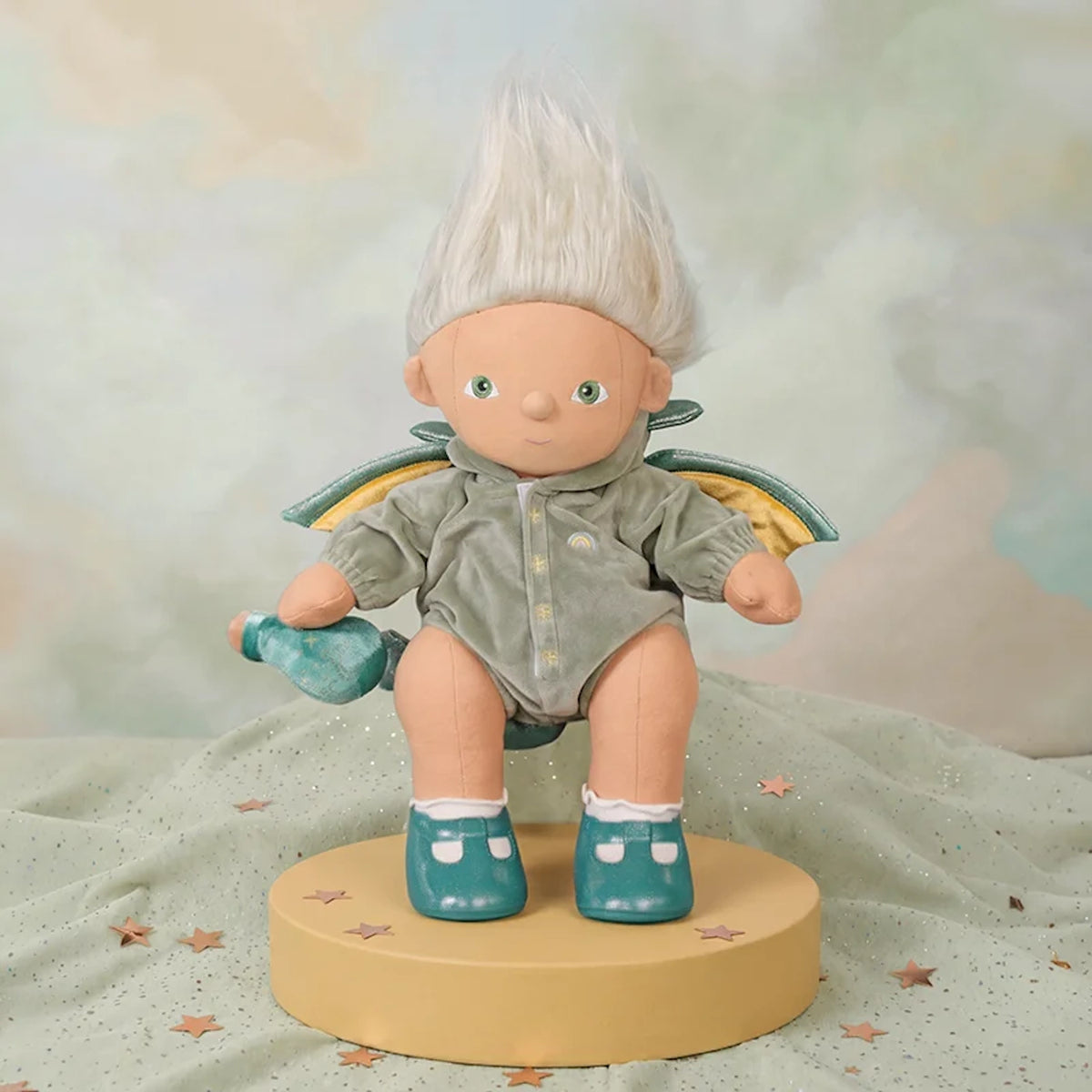 White-haired doll wearing green velvet dragon outfit on yellow pedestal with potion bottle in hand.