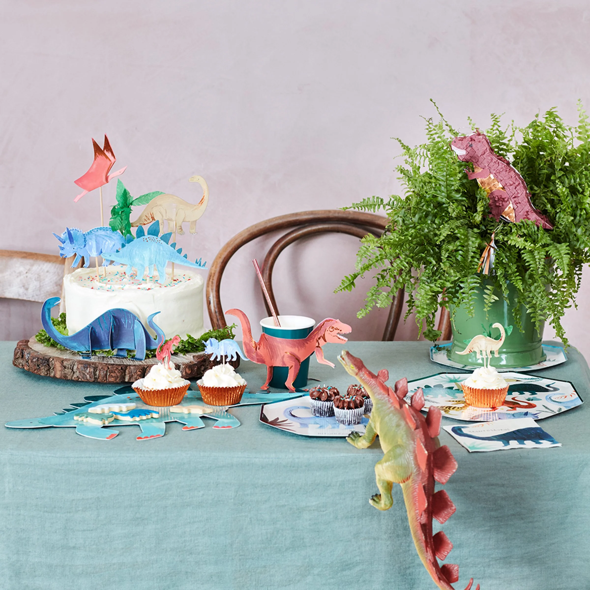 Birthday cake and cupcakes decorated with paper dinosaur toppers on a festive party table setup.