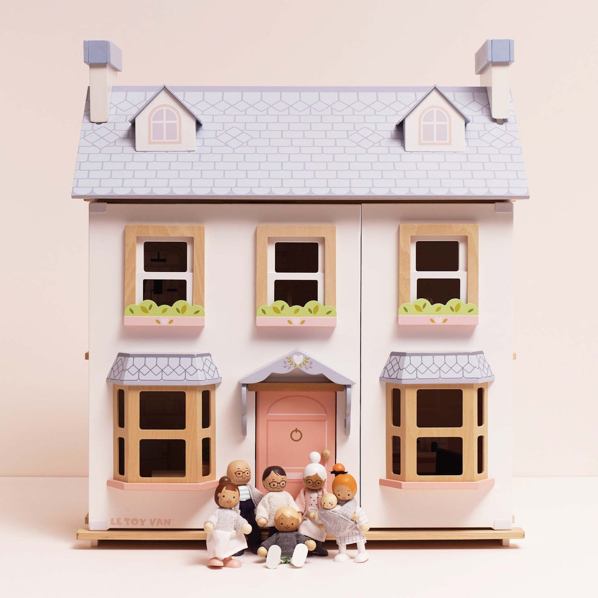 Seven wooden family figures gathered in front of a white dollhouse with a light blue roof.