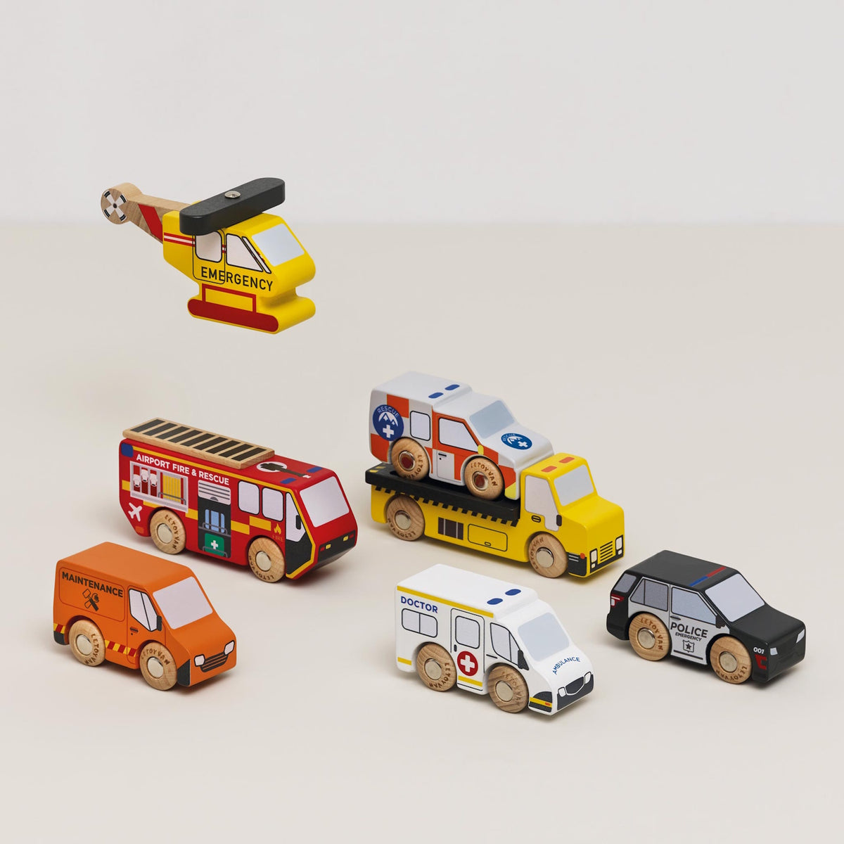 Wooden emergency toy vehicle set with a rescue car loaded on the flatbed truck and helicopter above.