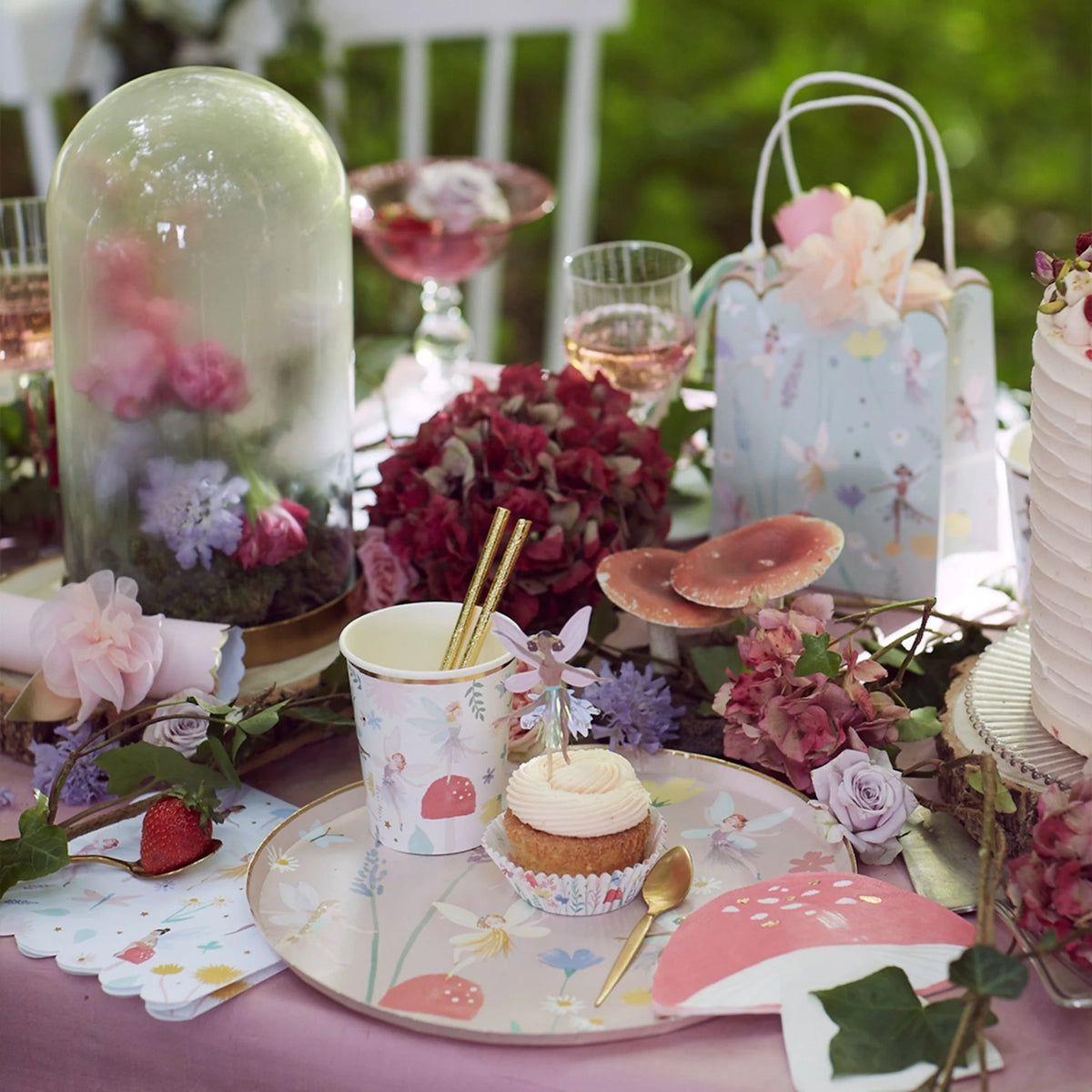 Fairy-themed party table with a cupcake, floral decor, mushroom details, and a glass cloche.