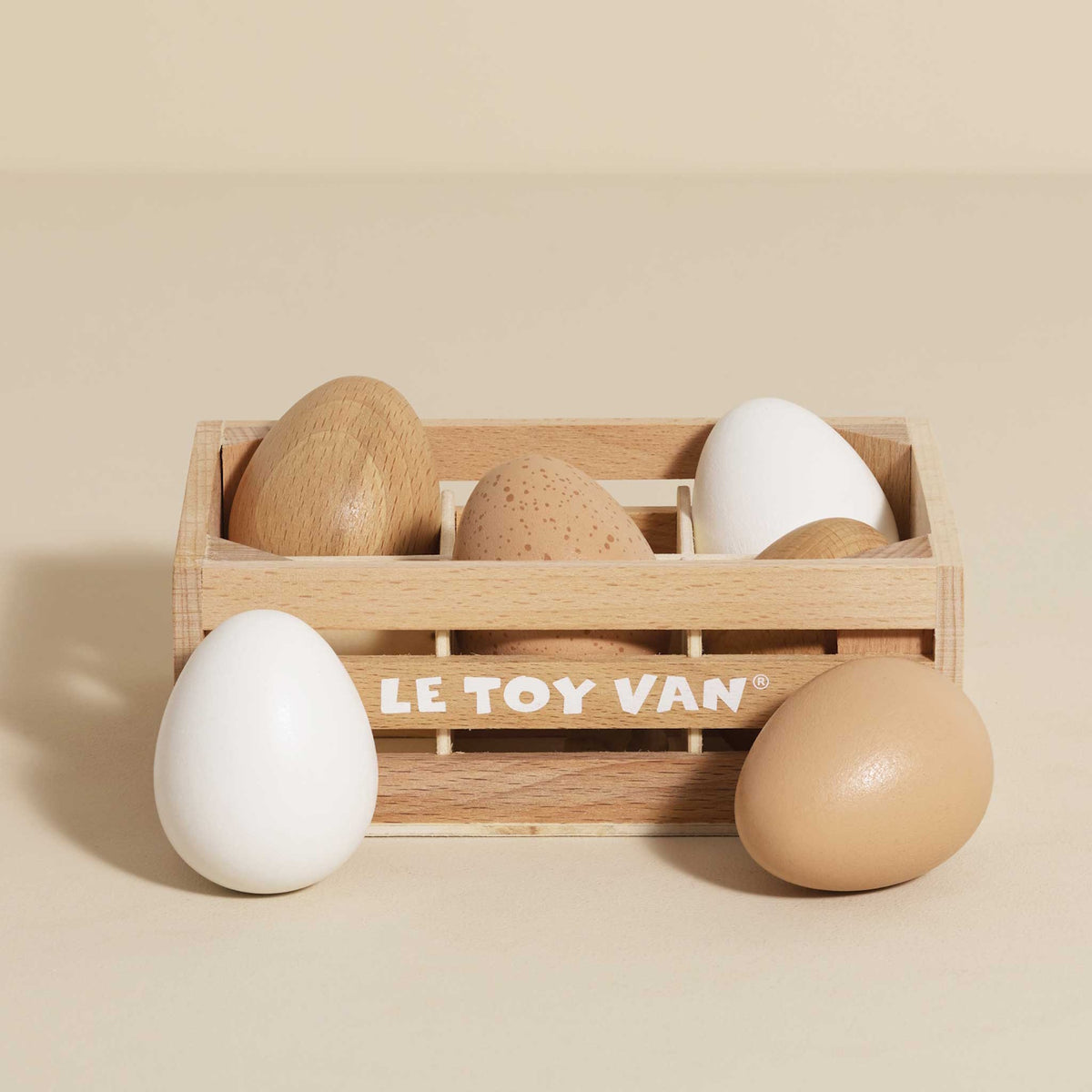 Wooden crate filled with toy eggs on a beige background.