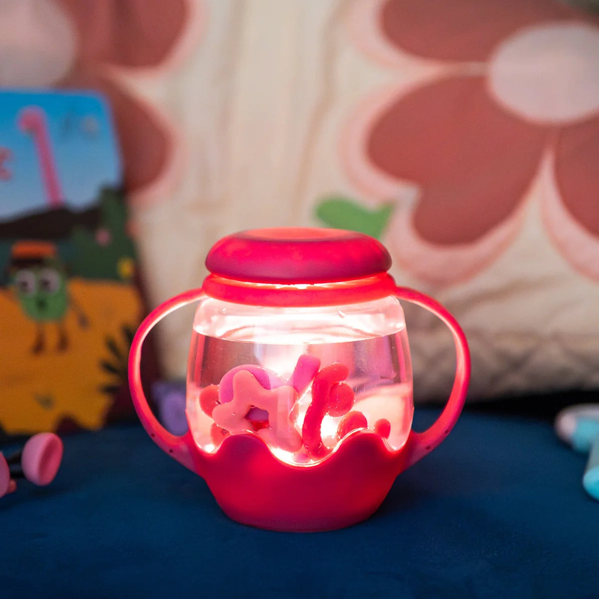 Glowing pink sensory jar with handles, filled with water and floating shapes on a dark surface.