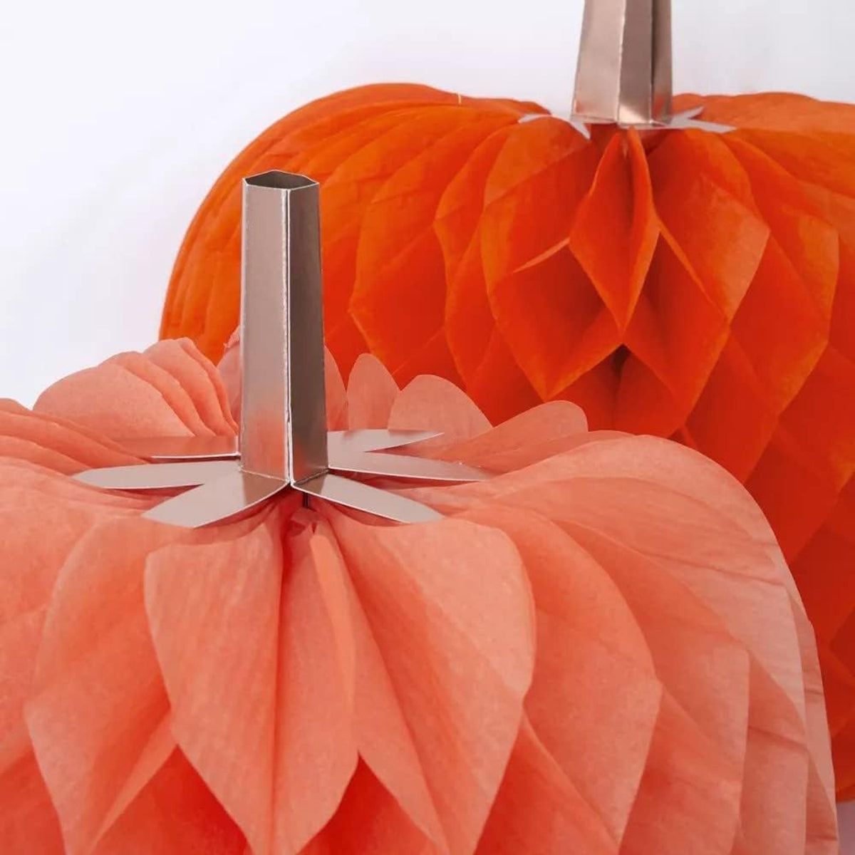 Close-up view of orange honeycomb tissue paper pumpkins with metallic copper stems.