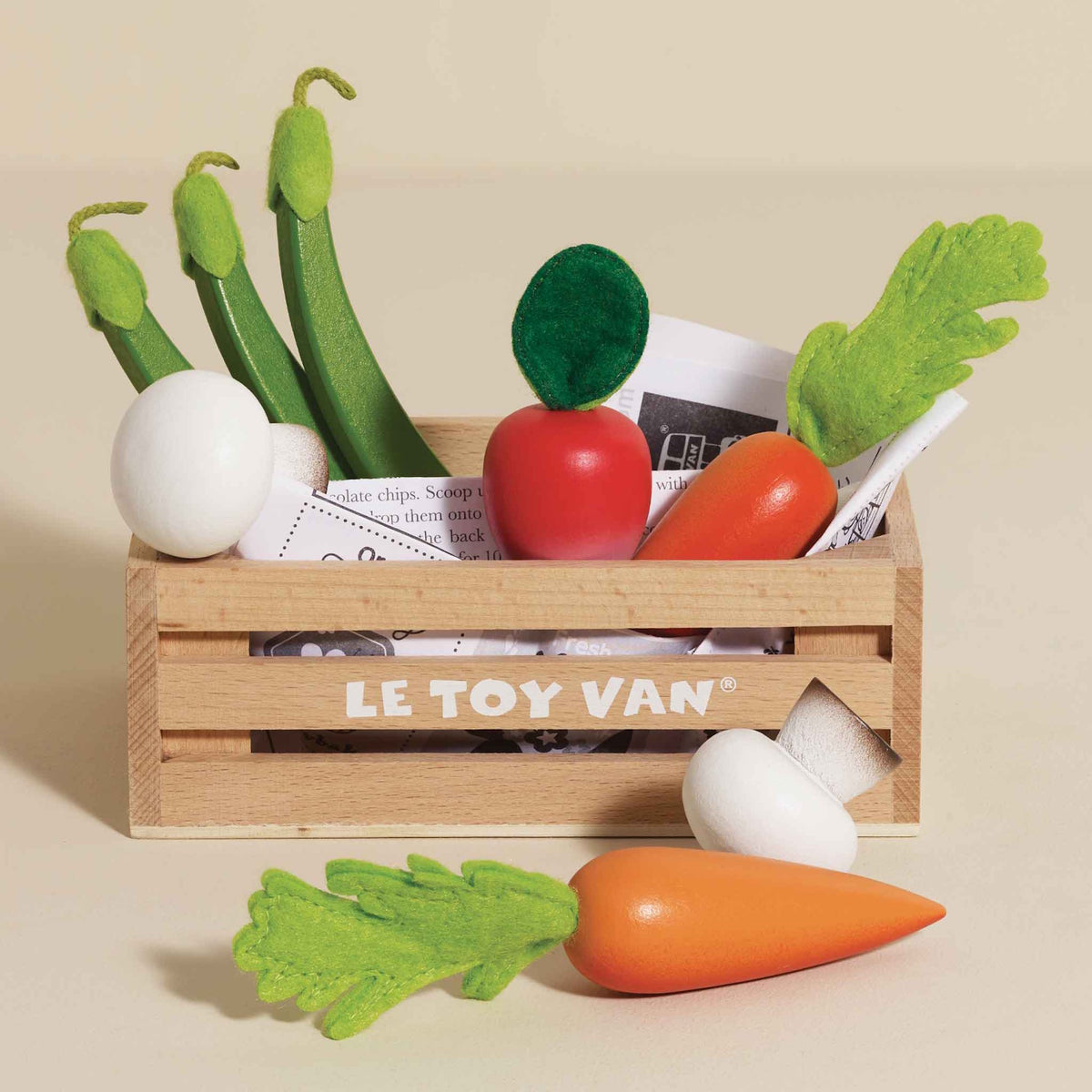 Wooden play vegetable set in a Le Toy Van crate with a carrot and mushroom in front, on beige background.