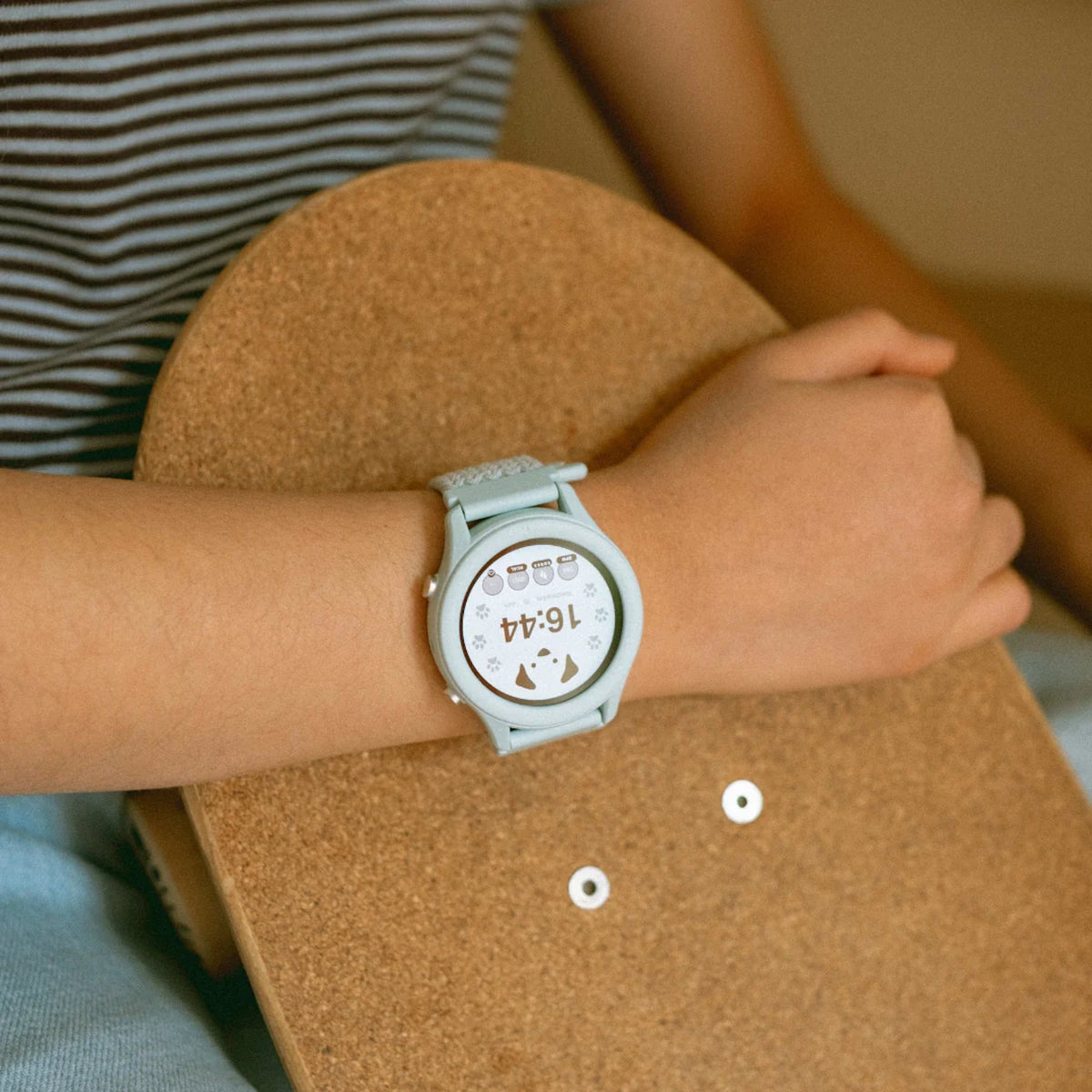Close-up of a person's wrist wearing a light blue smartwatch while holding a wooden skateboard.