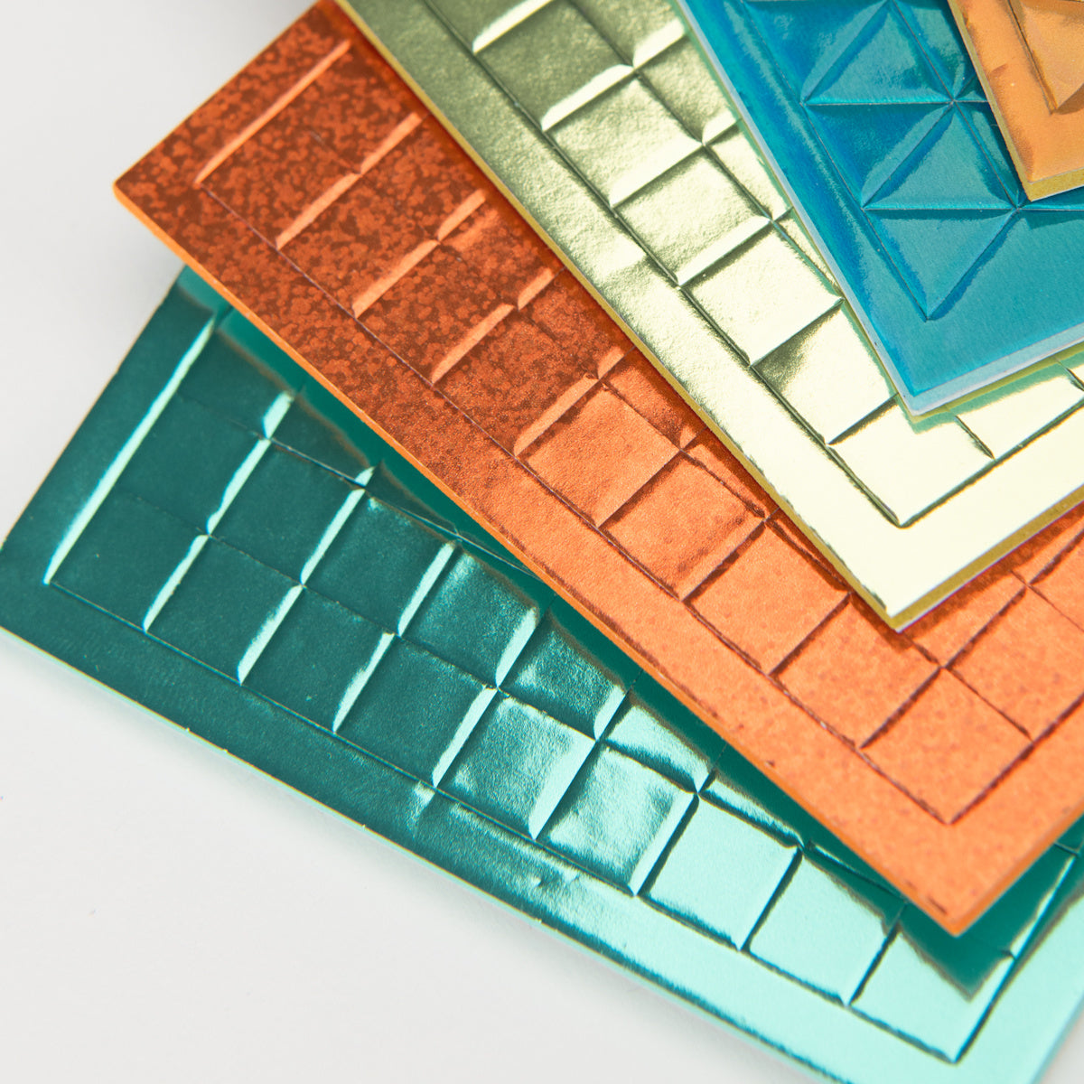 Stacked colorful metallic textured tiles with grid and geometric patterns on a white background.