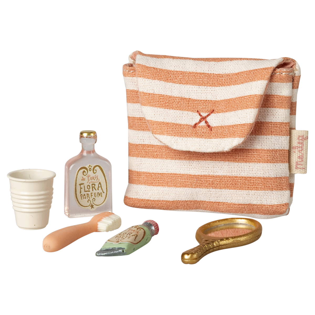 A small striped fabric pouch with a red cross is surrounded by a collection of miniature toiletries: a white cup, a perfume bottle, a toothbrush, a toothpaste tube, and a golden hand mirror, all against a white background.