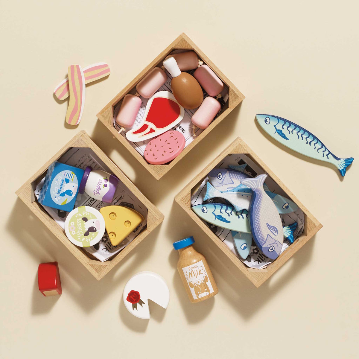 Three wooden crates filled with play food, including fish, meats, and dairy items on a beige surface.