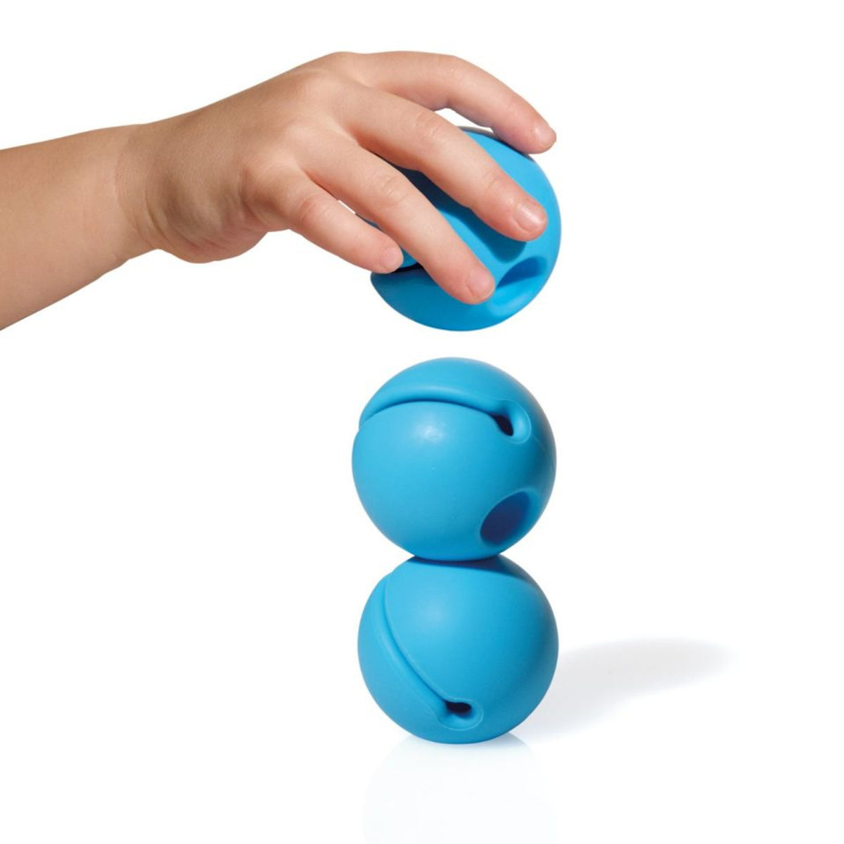 A child's hand places a blue ball on top of two stacked blue balls against a white background. The scene conveys focus and playfulness.