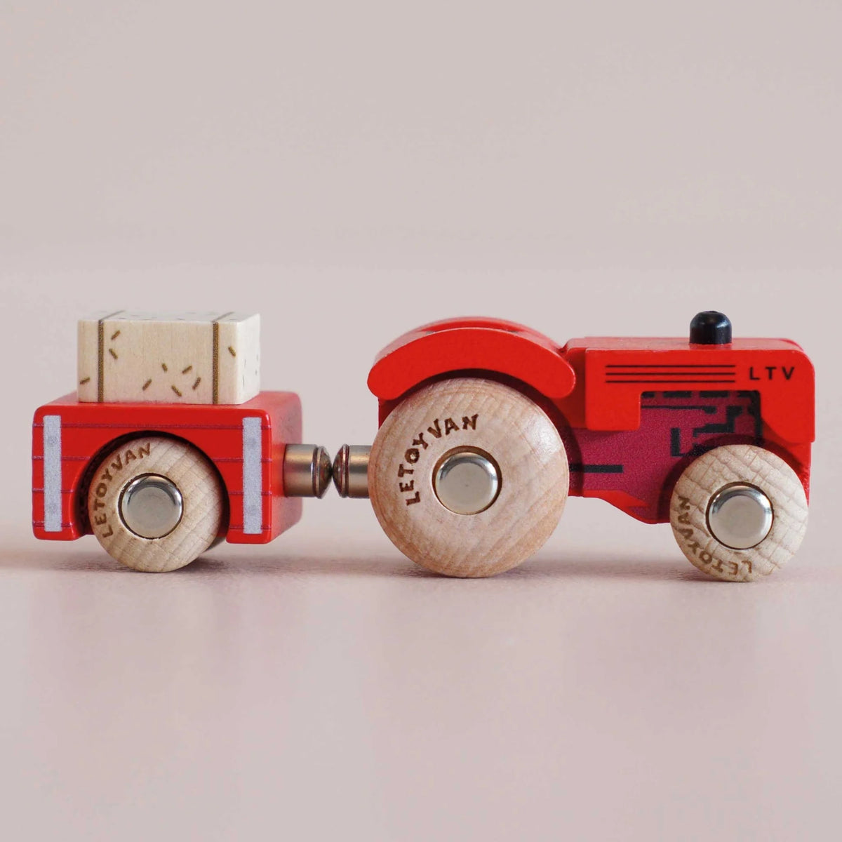 Red wooden toy tractor with trailer and hay bale, shown in a straight profile side view.