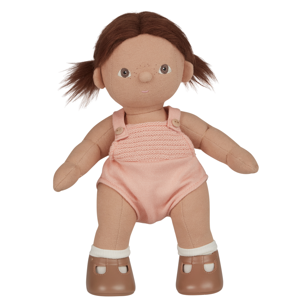 A soft, fabric doll with brown pigtails stands against a white background. It wears a pink romper and brown shoes, conveying a playful and charming tone.