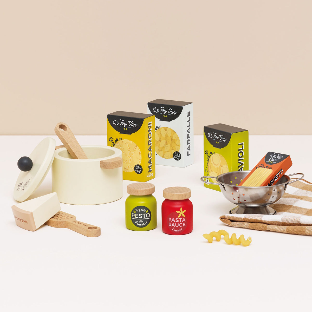 Wooden toy pasta play set with cooking pot, sauce jars, boxes, colander, and towel.