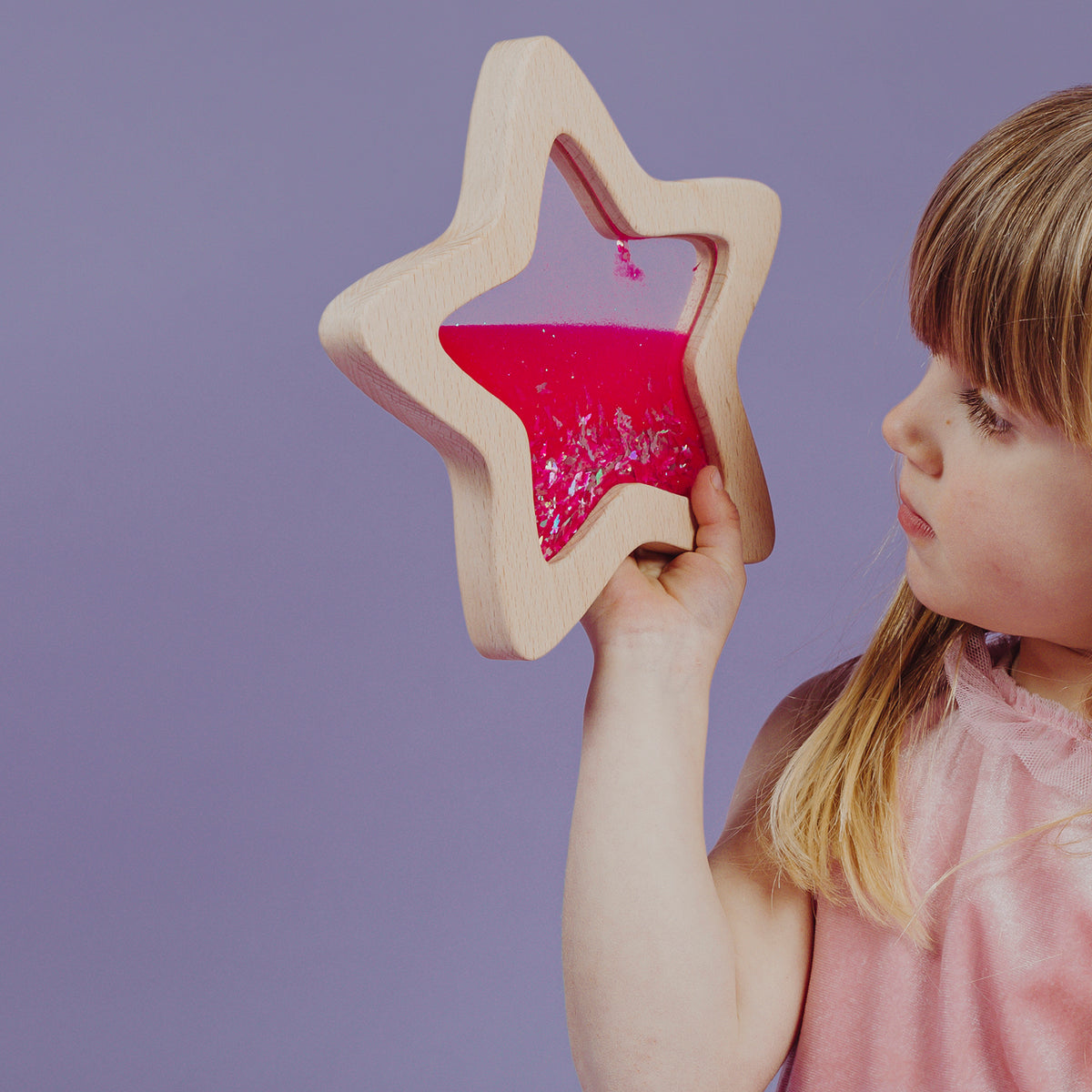 A young girl curiously looking through the pink glitter-filled star-shaped sensory toy.