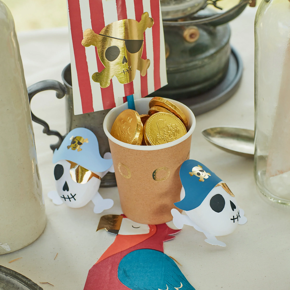 Pirate skull surprise balls, a cup filled with gold chocolate coins, and a pirate flag decoration on a table.