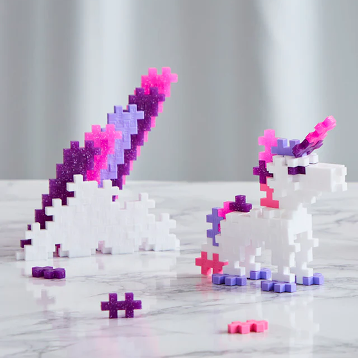 Plastic construction blocks form a white unicorn with pink and purple accents on a marble surface, conveying a playful and whimsical tone.
