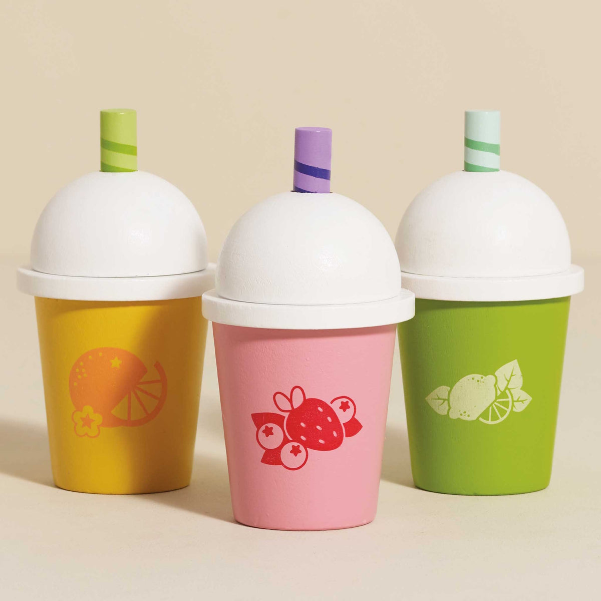 Three colorful wooden play smoothie cups with white domed lids on a beige backdrop.