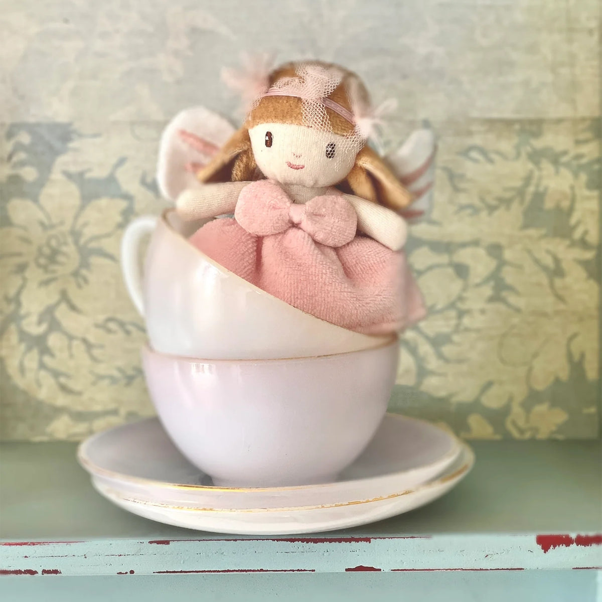 Small plush fairy doll in a pink dress sitting inside stacked vintage teacups.