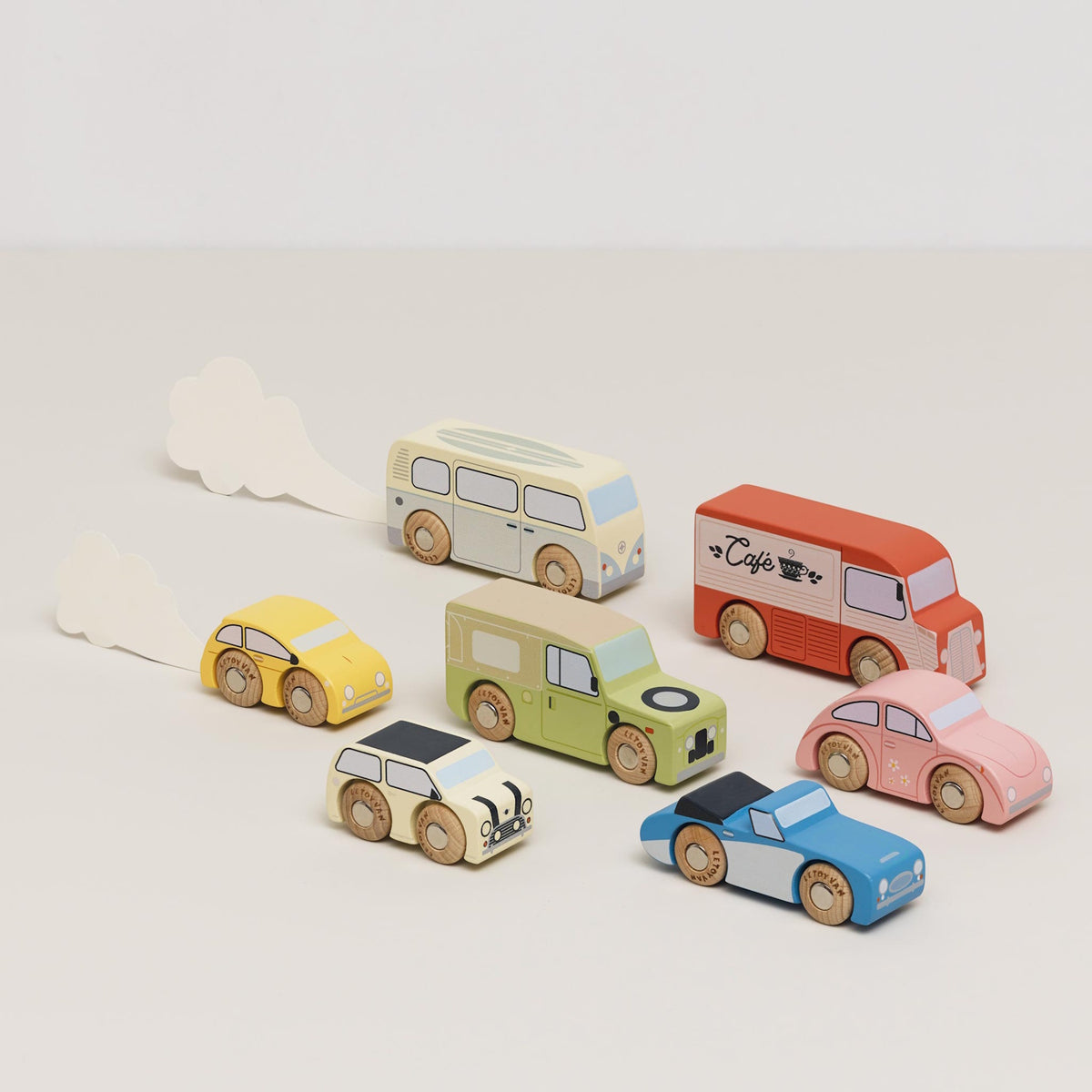 Seven vintage-style wooden toy vehicles driving on a beige surface, two with paper exhaust trails.