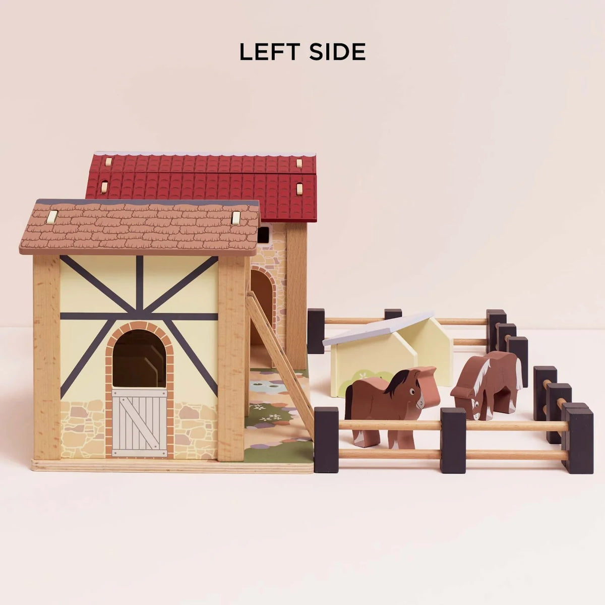 Left side view of the wooden farmyard stable playset with a half-timbered barn, horses, and a fence.