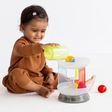 Side view of a toddler pouring a cup into a multi-colored translucent plastic toy carousel.