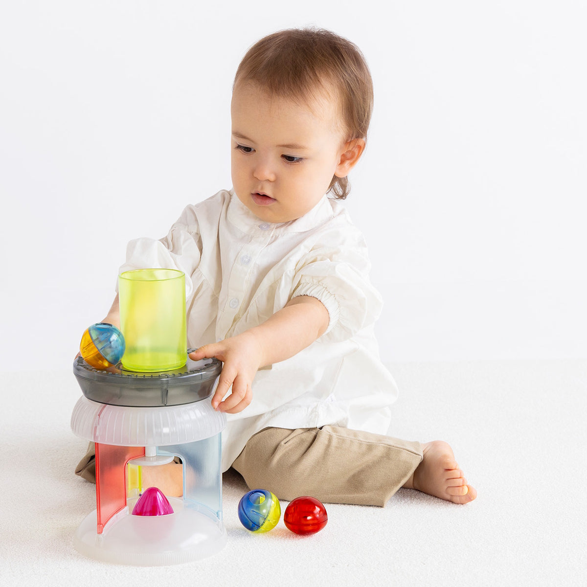 Angled front view of a toddler playing with an inverted multi-colored translucent plastic toy carousel.