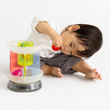 Front view of a toddler playing with a multi-colored translucent plastic toy carousel.