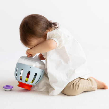 Side view of a toddler playing with an inverted light blue plastic toy curiosity lantern.