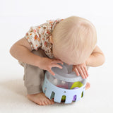 High-angle view of a toddler exploring an inverted light blue plastic toy curiosity lantern.