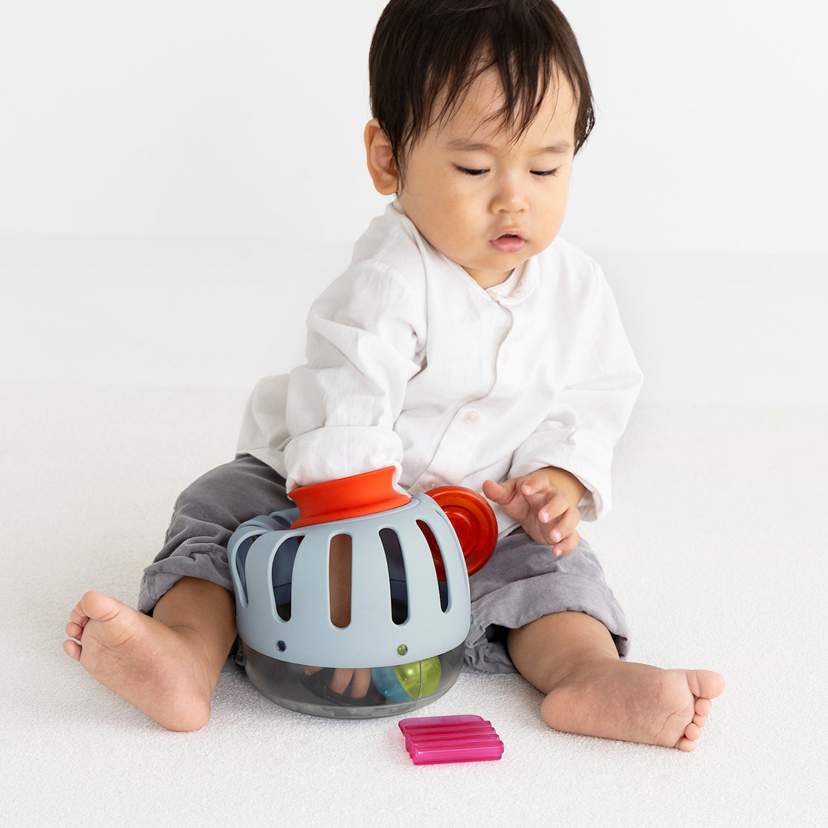 Front view of a toddler sitting and playing with a light blue plastic toy curiosity lantern.