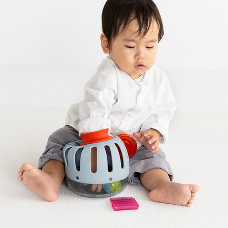 Front view of a toddler sitting and playing with a light blue plastic toy curiosity lantern.