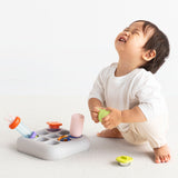 Front lifestyle view of a baby playing with the light gray silicone Curiosity Nook toy.