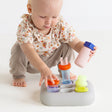 Front view of a toddler playing with the light gray silicone Curiosity Nook toy.