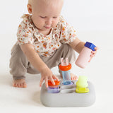 Front view of a toddler playing with the light gray silicone Curiosity Nook toy.