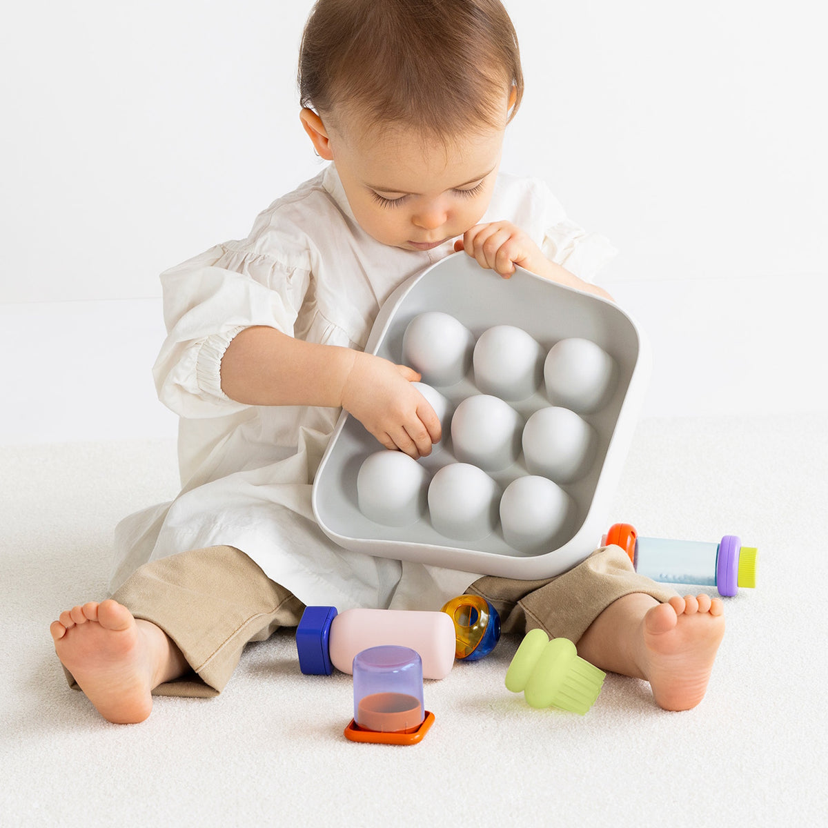 Front view of a toddler holding the light gray silicone Curiosity Nook toy.