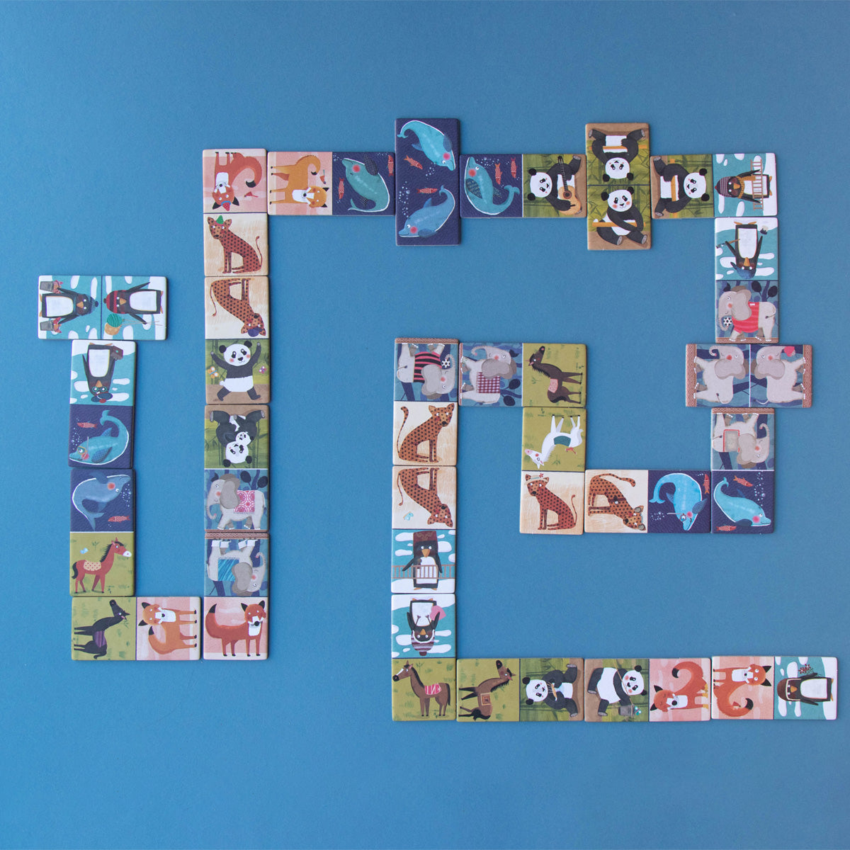 Penguins & Friends Domino pieces laid out in play – A set of beautifully illustrated animal domino pieces arranged in a game formation on a blue surface.