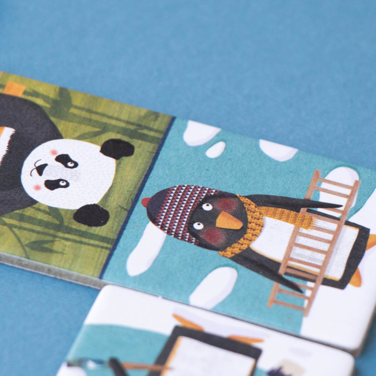 Close-up of Londji domino piece featuring a penguin with a wooden ladder – A penguin in a knitted hat carrying a wooden ladder, part of the Penguins & Friends Domino set.